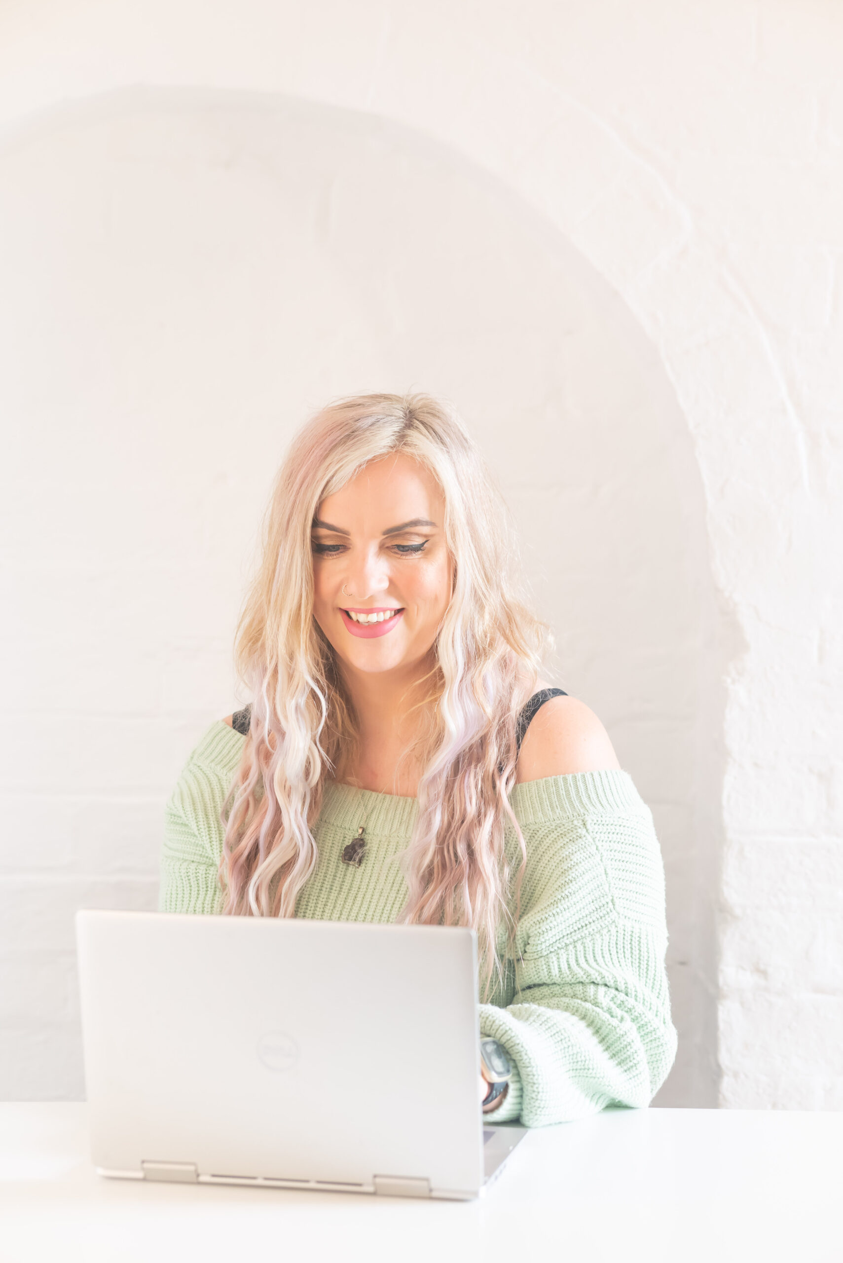 Laura Fish smiling while working on her laptop, representing Fashion Toolbox’s friendly, expert-led approach to digital fashion services